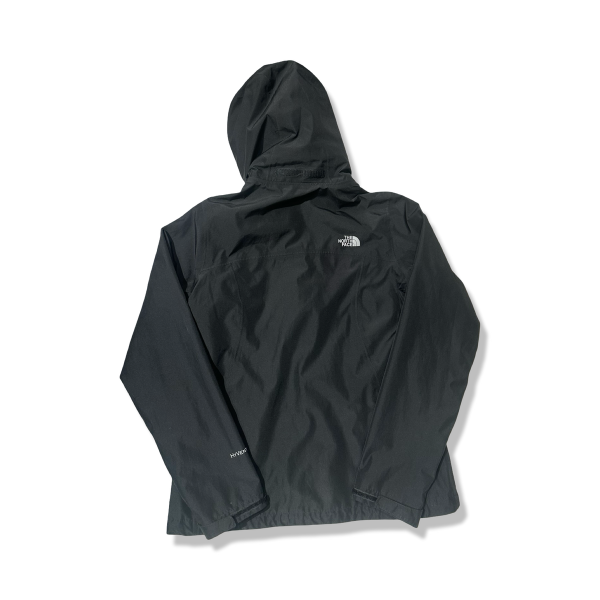 Baksidan av en svart skaljacka för dam från The North Face med huva, fotograferad mot en vit bakgrund.