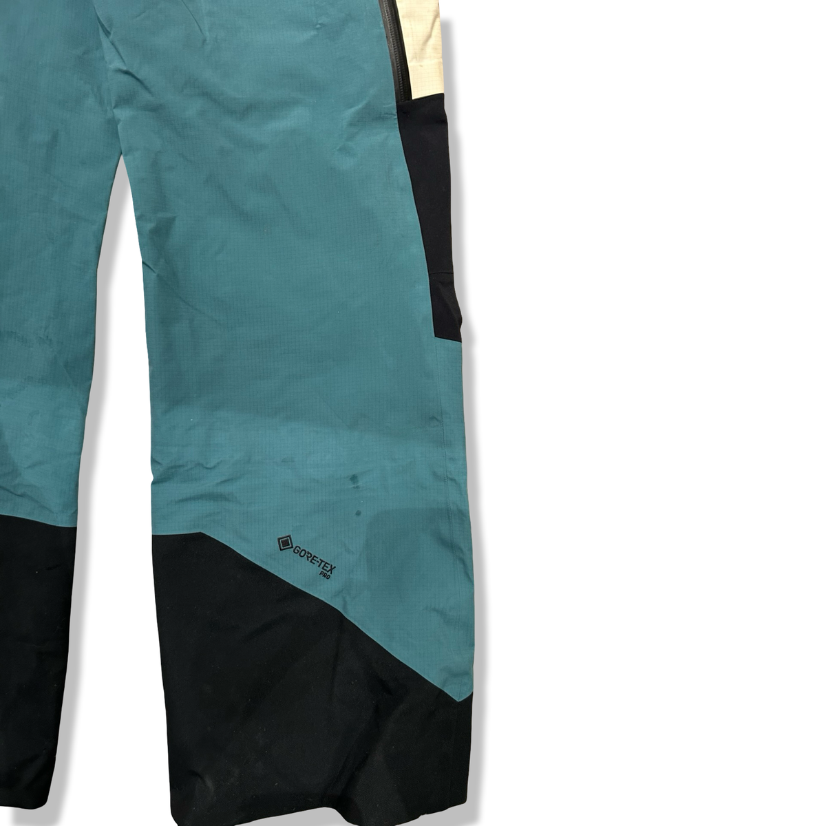 Close-up of a blue and white Peak Performance shell pants with black details and Gore-Tex Pro logo against a white background.
