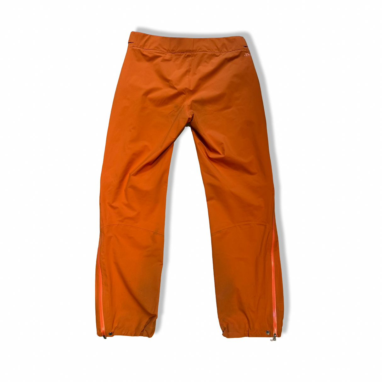 Baksidan av orange Houdini BFF Pants regnbyxor för dam, fotograferade mot en vit bakgrund.