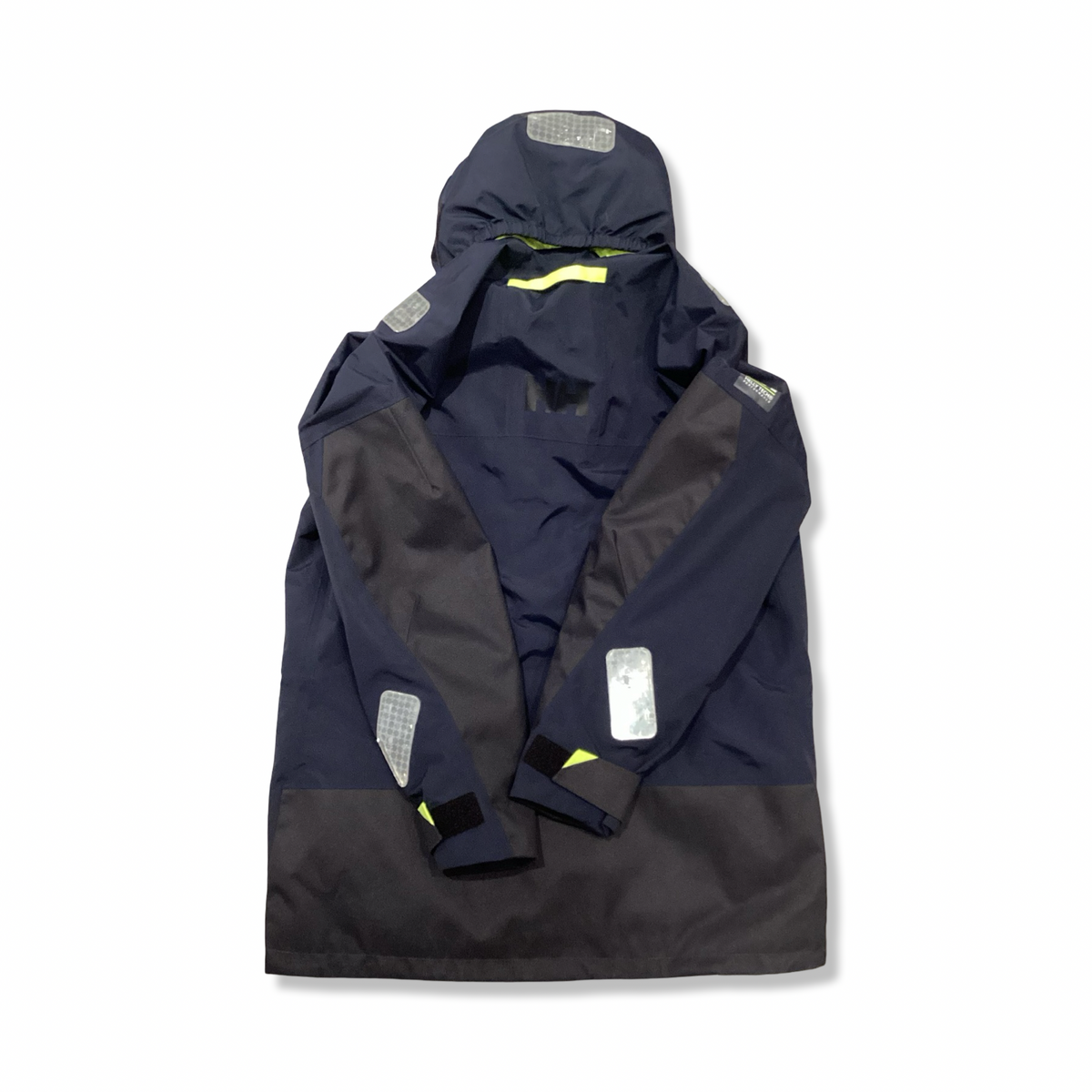 Baksidan av en blå Helly Hansen seglarjacka för dam med huva och reflexdetaljer, fotograferad mot en vit bakgrund.