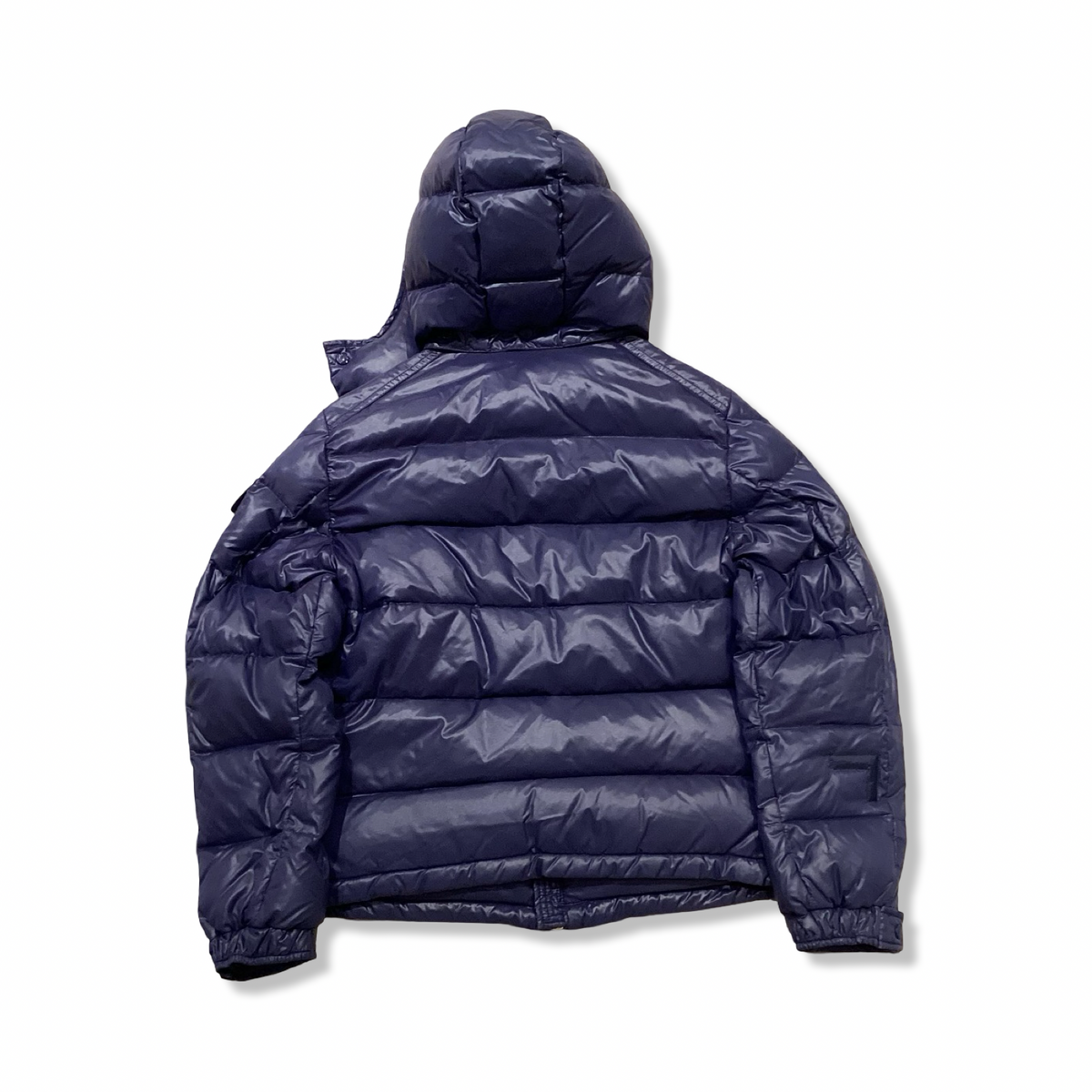 Baksidan av en blå dunjacka från Moncler för barn med huva, fotograferad mot en vit bakgrund.