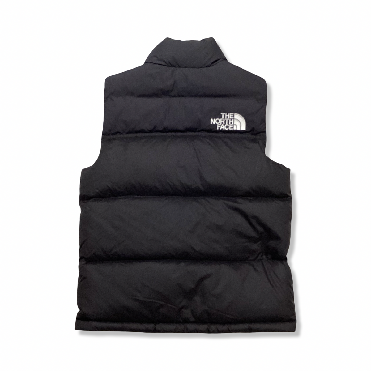 Baksidan av en svart väst från The North Face för barn, fotograferad mot en vit bakgrund.