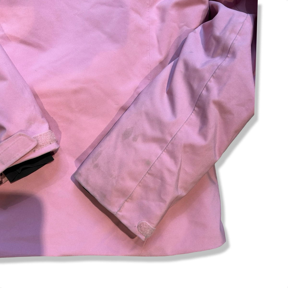 Close-up of the sleeve on the pink Peak Performance ski jacket with visible stains against a white background.