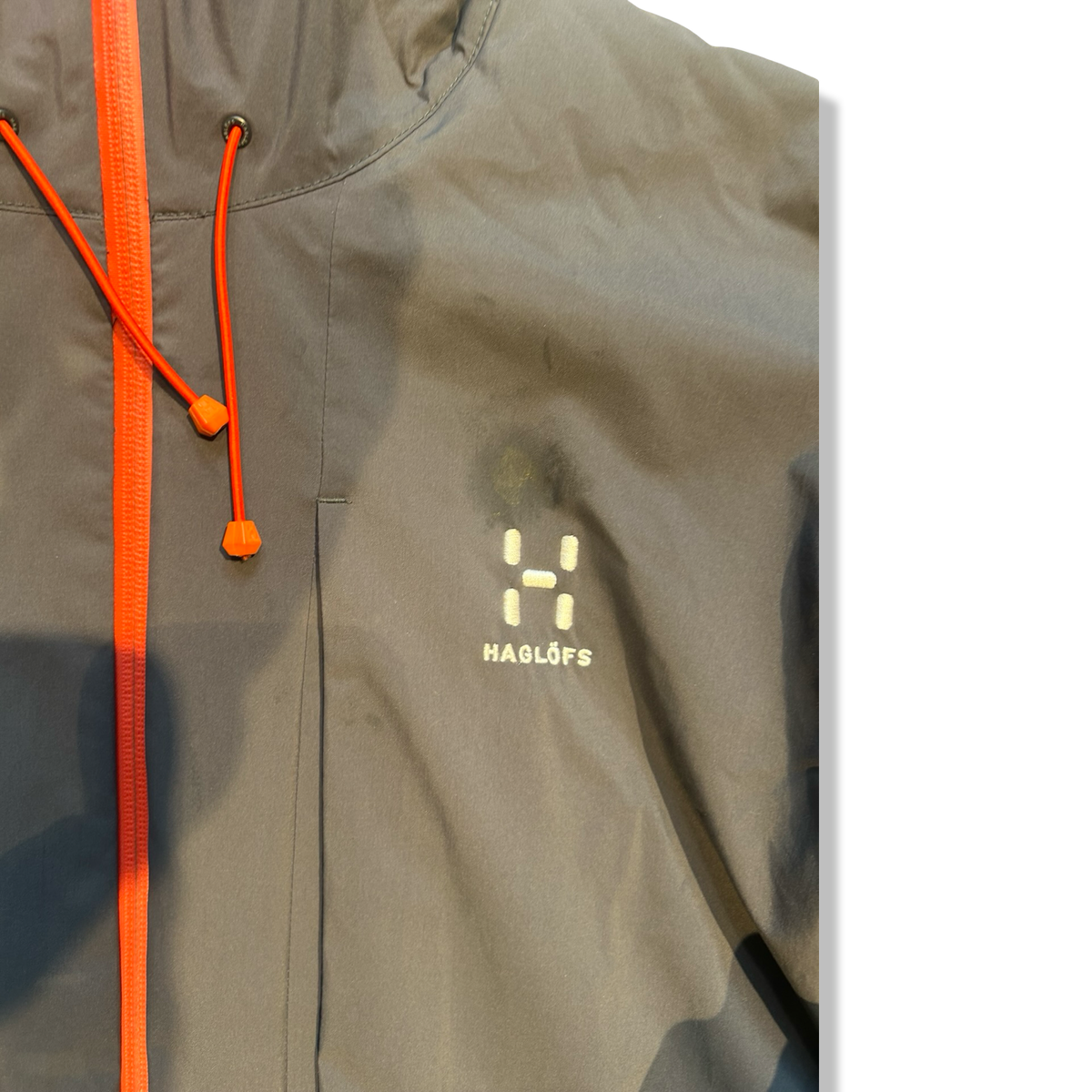 Close-up of a grey Haglöfs men's hybrid jacket showing a stain near the logo, front view.