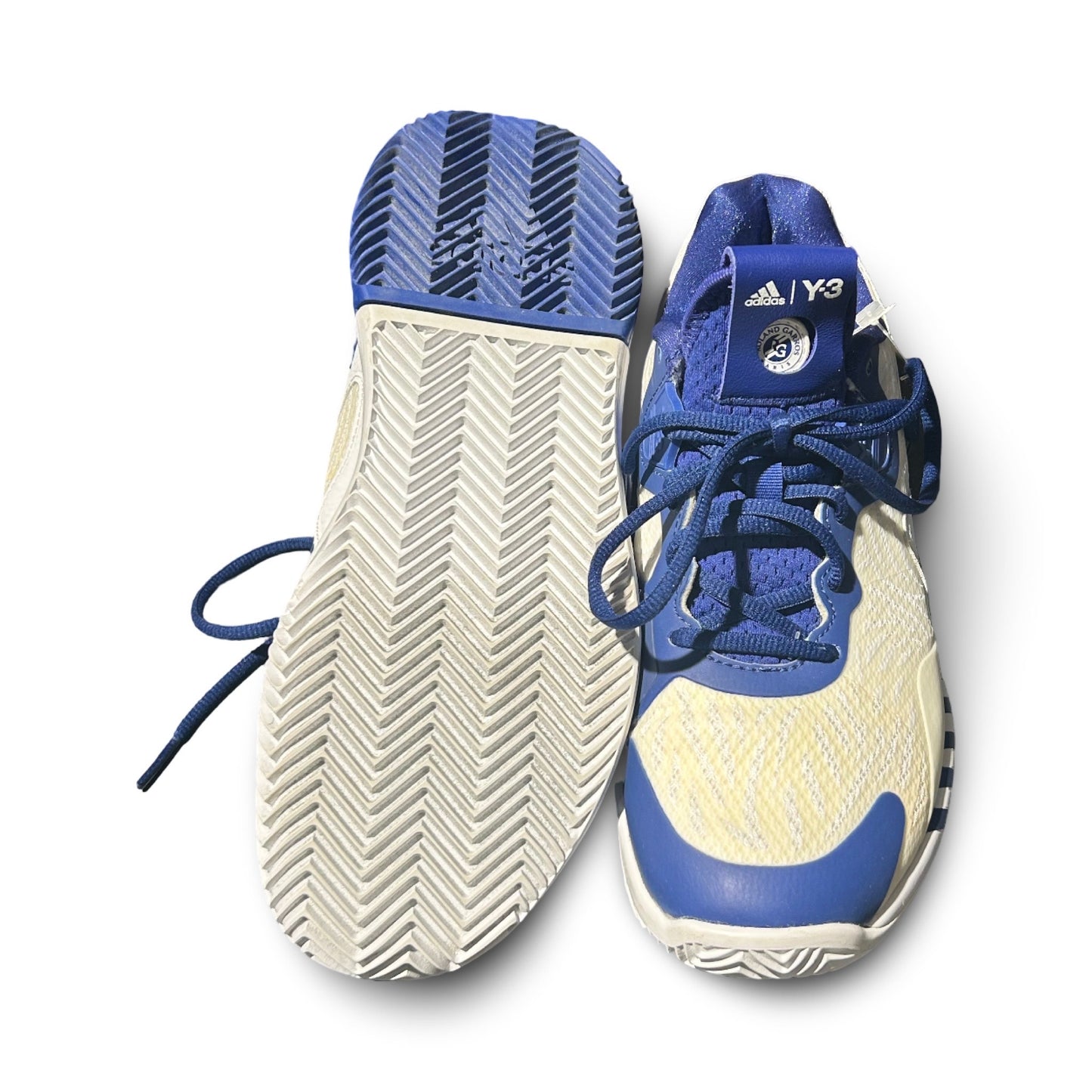 Ett par Adidas Y-3 Adizero Roland Garos tennisskor för dam i vitt och blått, där ena skon visas uppifrån och den andra visar sulan. Fotograferade platt mot en vit bakgrund.