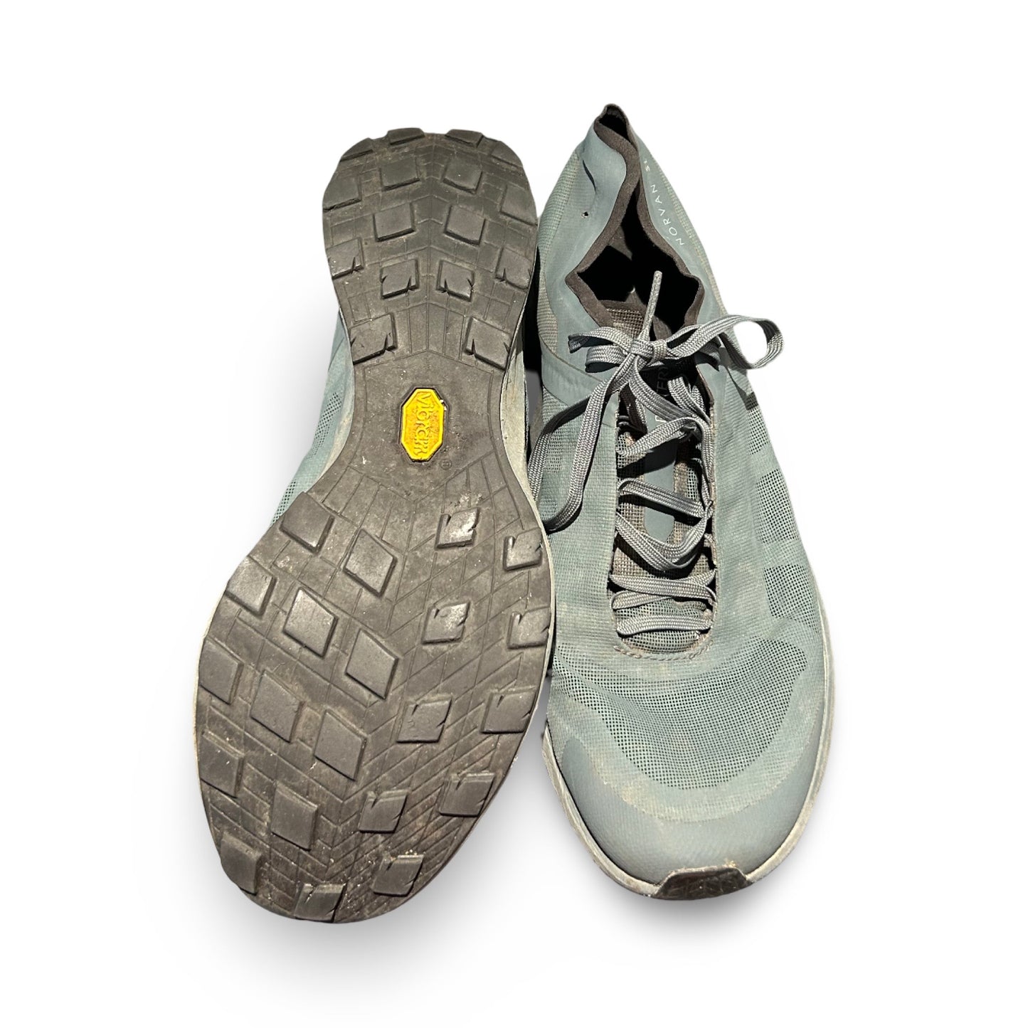 Ett par Arc'teryx Norvan löparskor i grått, där ena skon visas uppifrån och den andra visar sulan, fotograferade mot en vit bakgrund.