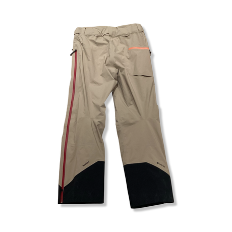 Back view of a beige Peak Performance men's shell pants with black reinforcements against a white background.
