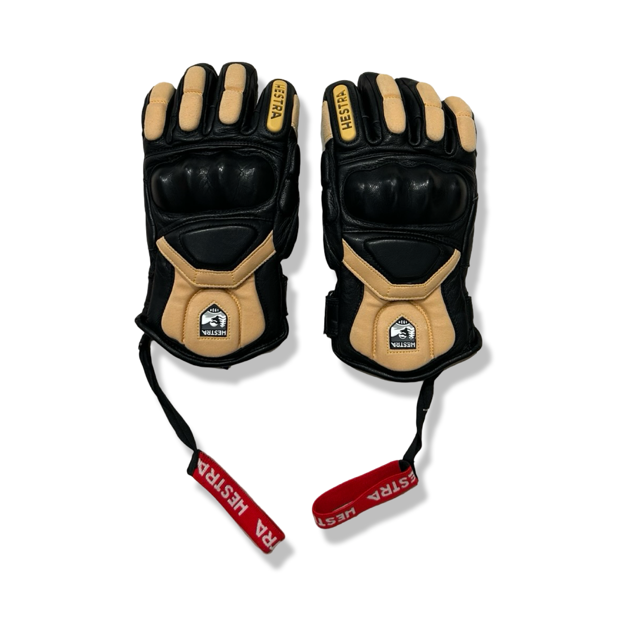 A pair of brown and black Hestra gloves with protective panels and red logo straps, photographed against a white background.