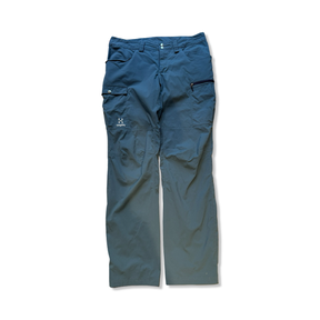 Blå funktionsbyxor för herr från Haglöfs med fickor och logotyp, fotograferade framifrån mot vit bakgrund.