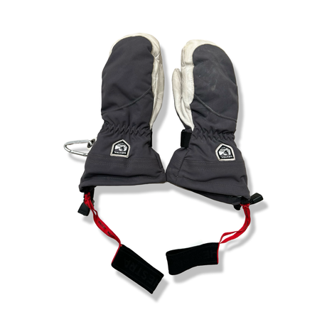 A pair of blue and white Hestra mittens with wrist straps and a carabiner, photographed against a white background.