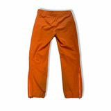 Baksidan av orange Houdini BFF Pants regnbyxor för dam, fotograferade mot en vit bakgrund.