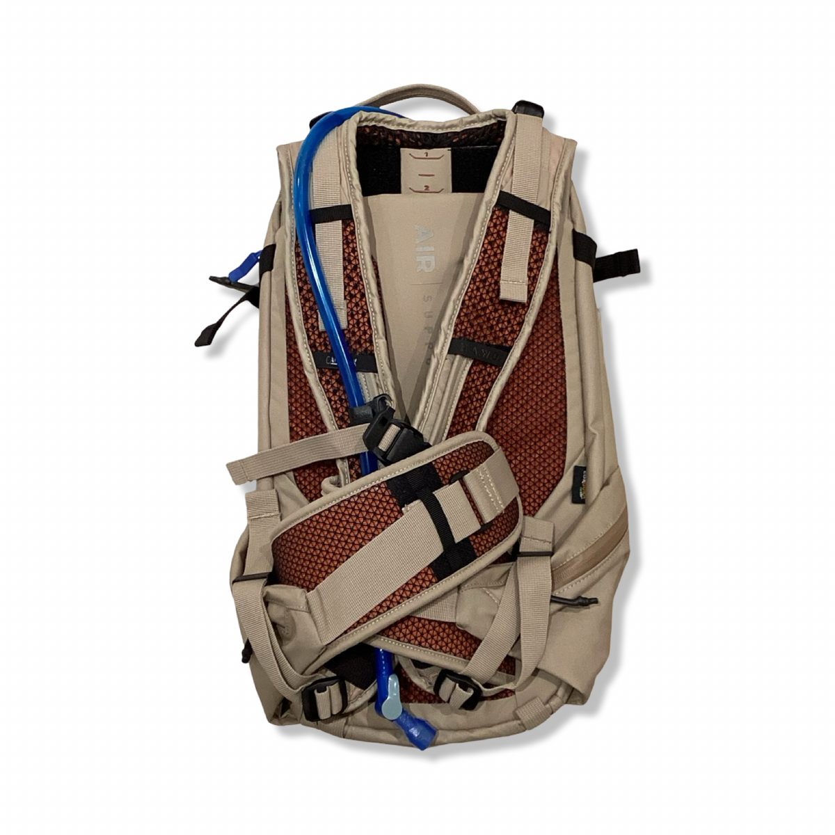 Baksidan av en beige Camelbak HAWG 20 L ryggsäck med vadderat bärsystem och blå vätskeslang, mot vit bakgrund.