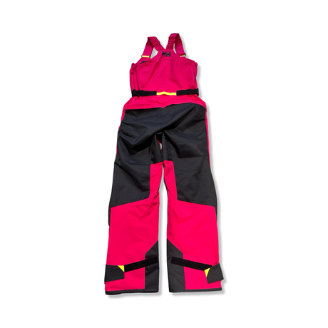 Rosa och svarta Helly Hansen W Skagen Offshore Bib seglarbyxor för dam, fotograferade bakifrån mot vit bakgrund.