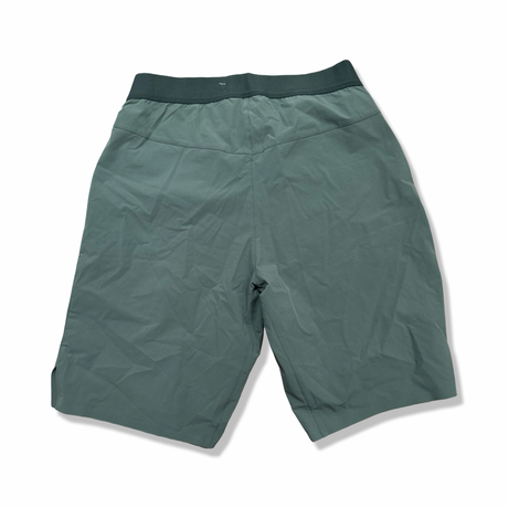 Baksidan av ett par gröna Salomon Wayfarer Pull On Short funktionsshorts för herr, fotograferade mot en vit bakgrund.