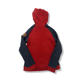 Baksidan av en röd och mörkblå fleecehoodie från Peak Performance för dam, fotograferad mot en vit bakgrund.