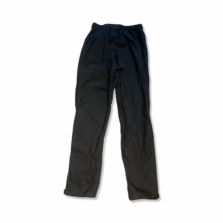 Black Marmot rain pants in crinkly fabric with an elastic waist and adjustable cuffs against white.