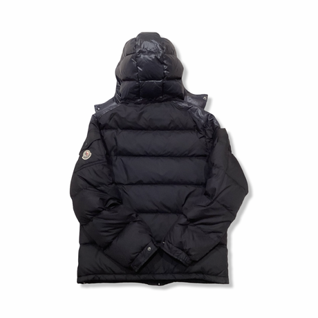 Baksidan av en blå dunjacka från Moncler med huva, fotograferad mot en vit bakgrund.