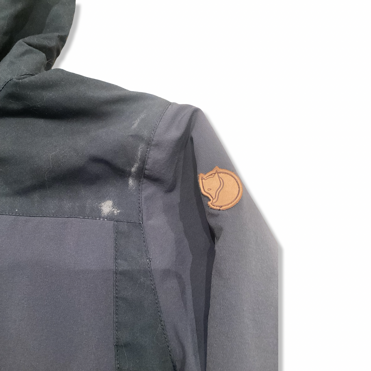 Close-up of the sleeve and shoulder of a blue Fjällräven rain jacket with a leather logo.