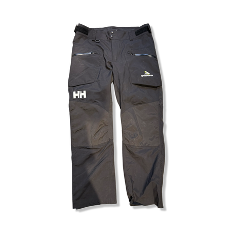 Svart Helly Hansen HP Foil seglarbyxa för herr med dragkedja och förstärkta knän, fotograferad framifrån mot en vit bakgrund.