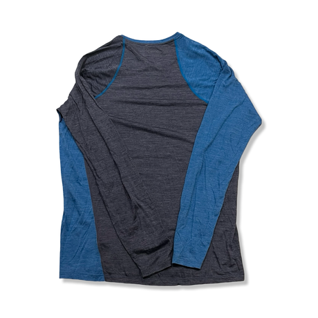 Back view of a blue and dark grey Ortovox men's Rock'N'Wool Long Sleeve base layer top against a white background.