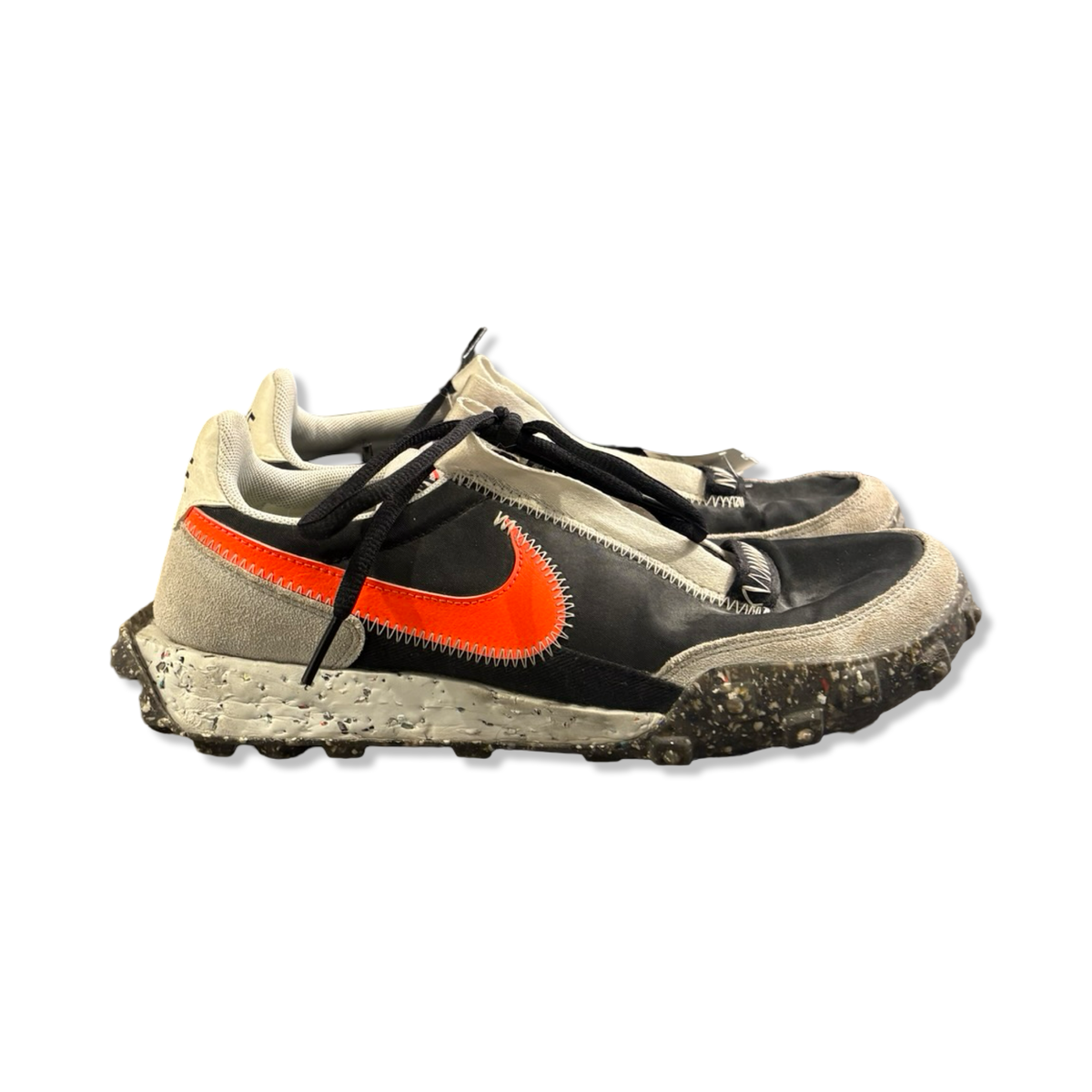Grey and black Nike Waffle Racer Crater women's running shoes with an orange swoosh, photographed from the side against a white background.