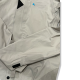 Close-up of a beige and gray Klättermusen down jacket with an embroidered logo on the chest.