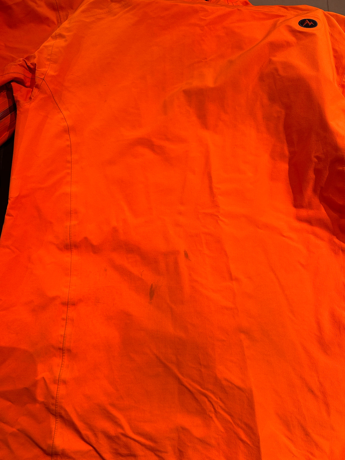 Close-up of the back of an orange Marmot men's shell jacket, showing stains on the back.