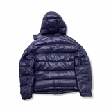 Baksidan av en blå dunjacka från Moncler för barn med huva, fotograferad mot en vit bakgrund.