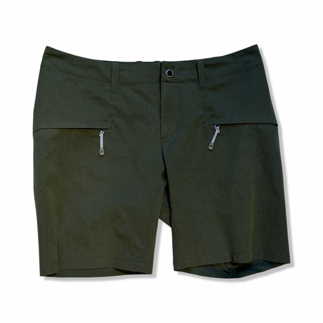 Gröna Houdini Daybreak shorts för dam med dragkedjefickor, fotograferade framifrån mot en vit bakgrund.