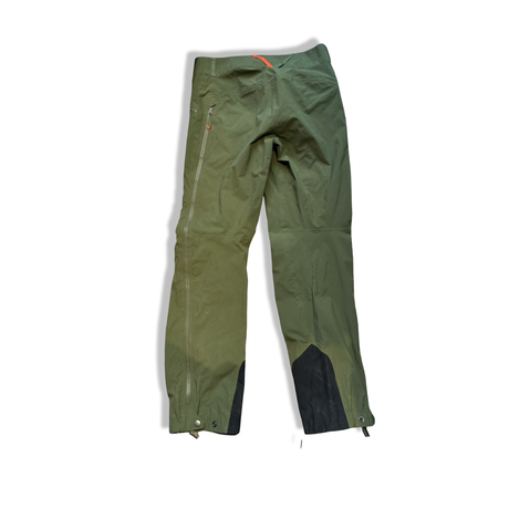 Back view of green Haglöfs Evo Grym unisex shell pants with side zippers and reinforced leg ends against a white background.