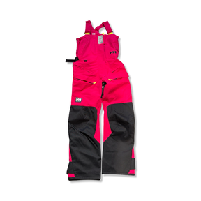 Rosa och svarta seglarbyxor från Helly Hansen i W Skagen Offshore Bib-modell för dam, visade mot vit bakgrund.