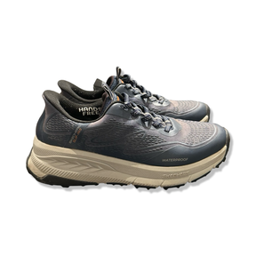 Ett par blå Skechers löparskor med tjock ljusbrun sula, fotograferade från sidan mot en vit bakgrund.