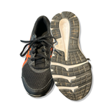 Black Asics women's running shoes with orange details and laces, one showing a worn outsole on white.