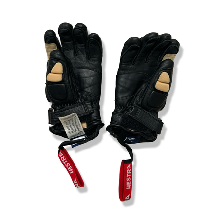 A pair of black Hestra gloves with red straps and beige details, photographed against a white background.