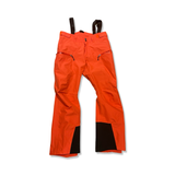 Orange skalbyxa Bergans Stranda 2L pants för dam med hängslen och svarta förstärkningar, fotograferad framifrån mot en vit bakgrund.