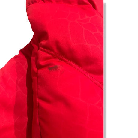 Close-up of a stain on the left sleeve of a red Columbia women's down jacket against a white background.