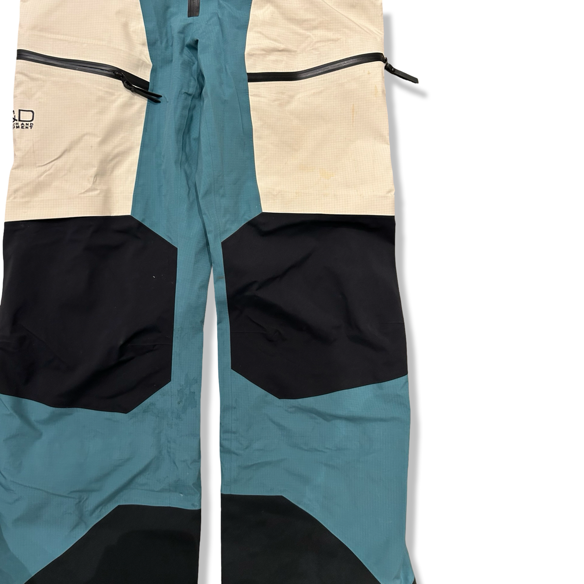 Close-up of the Peak Performance Vertical shell pants in blue, white, and black with details and zippers.