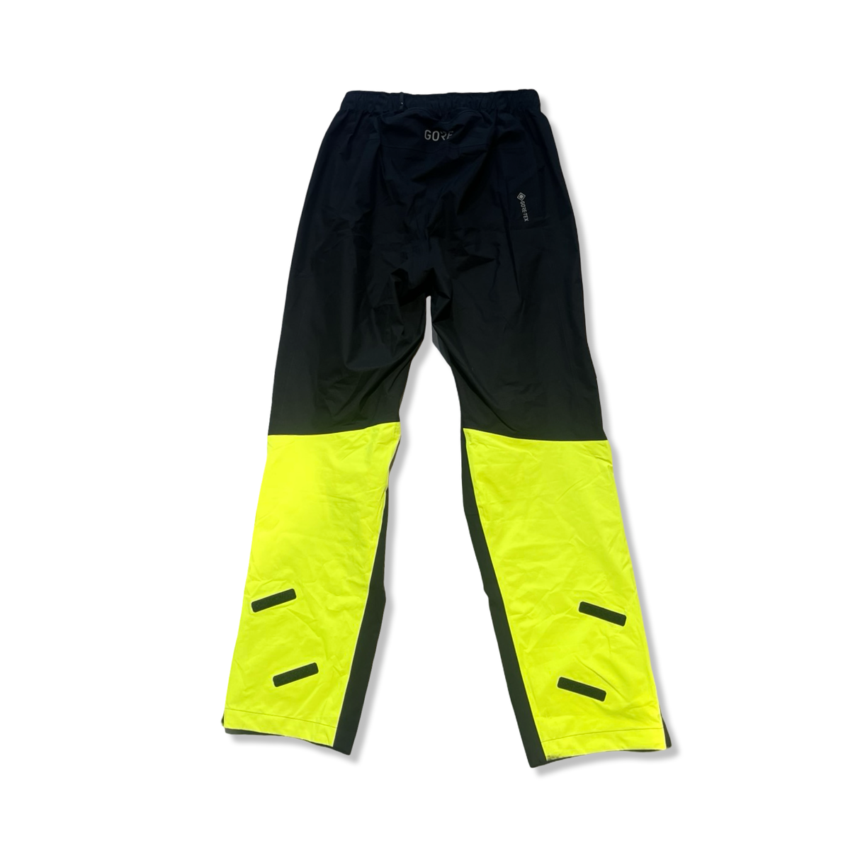 Svarta Gore Wear-regnbyxor med neongula benslut och Gore-Tex-märkning, fotograferade mot vit bakgrund.