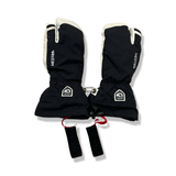 A pair of black and white Hestra three-finger gloves with wrist straps, front view against a white background.