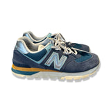 Blå New Balance sneakers för herr i mocka med silverdetaljer, fotograferade från sidan mot vit bakgrund.