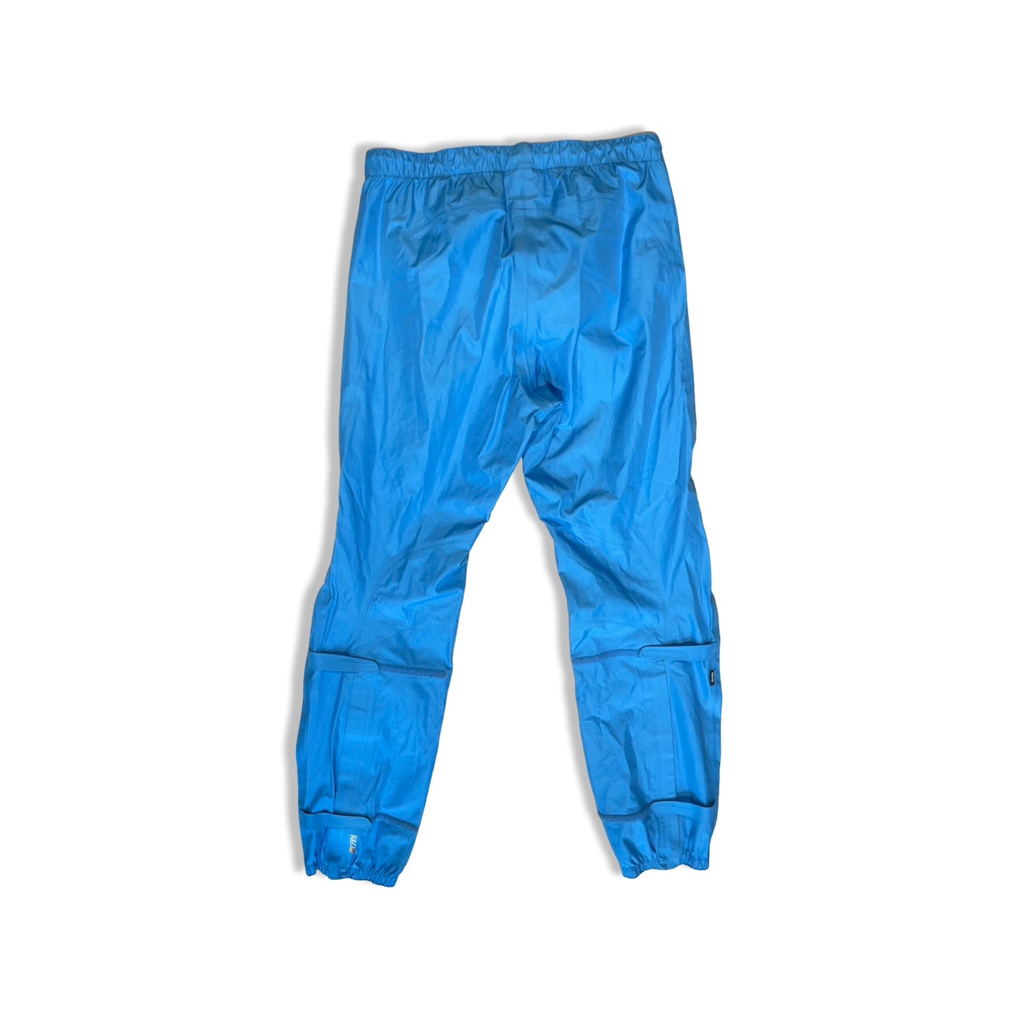 Blå Peak Performance Stark Pant skalbyxor för dam, fotograferade bakifrån mot en vit bakgrund.