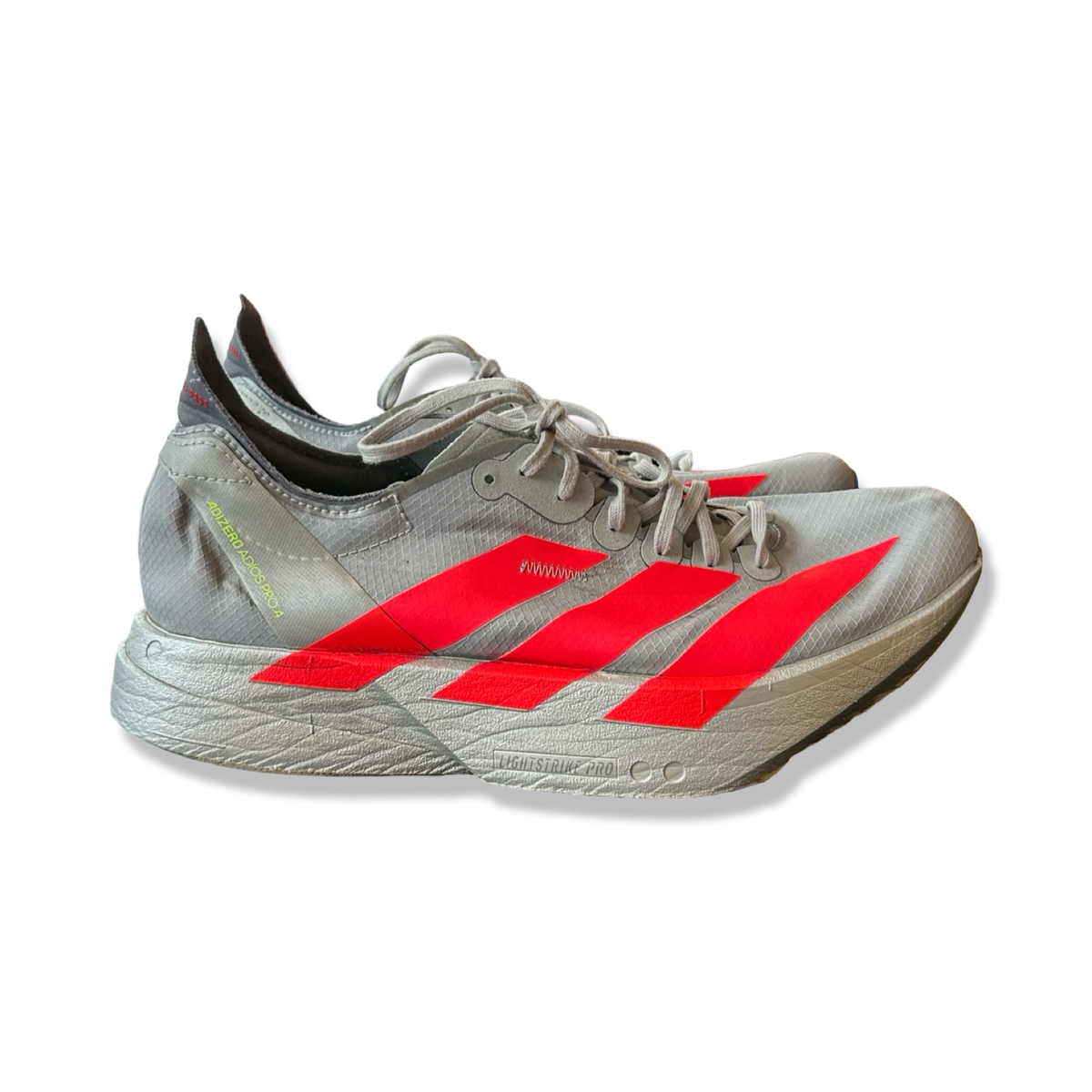 Grå löparskor Adidas Adizero Adios Pro 4 för dam med röda detaljer, fotograferade från sidan mot en vit bakgrund.