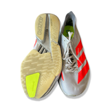 Grå löparskor Adidas Adizero Adios Pro 4 för dam med röd dekor, där ena skons sula visas underifrån mot en vit bakgrund.