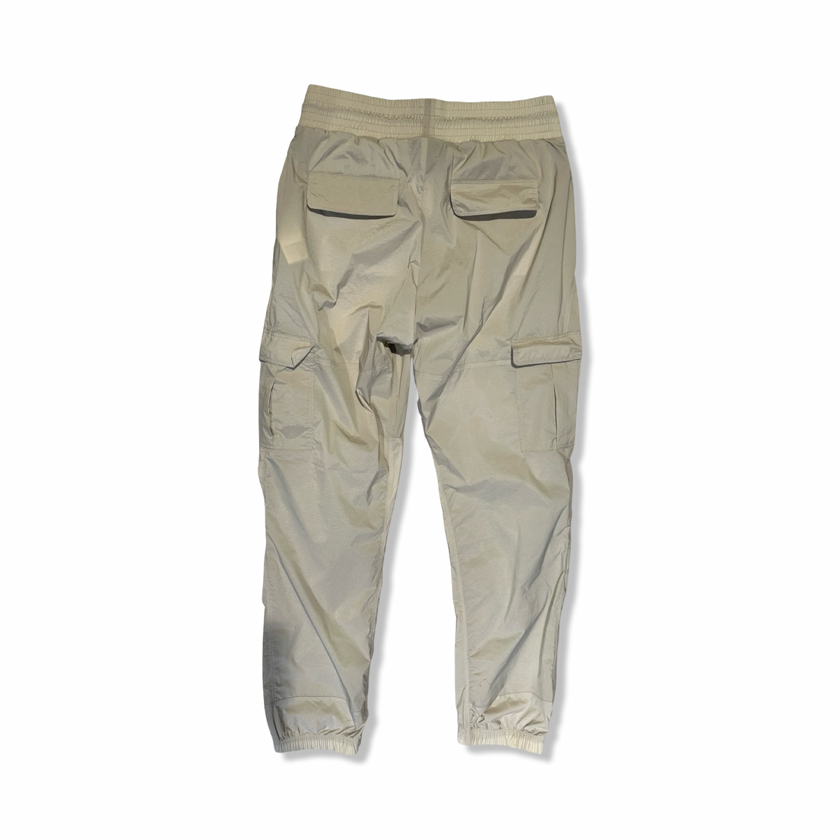 Baksidan av beige funktionsbyxor från Peak Performance för dam med fickor, fotograferade mot en vit bakgrund.