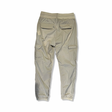 Baksidan av beige funktionsbyxor från Peak Performance för dam med fickor, fotograferade mot en vit bakgrund.