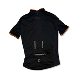 Women's black Triban cycling jersey with orange details, back view showing rear pockets on a white background.