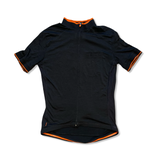 Women's Triban black short-sleeved cycling jersey with orange accents and zipper, front view on white background.
