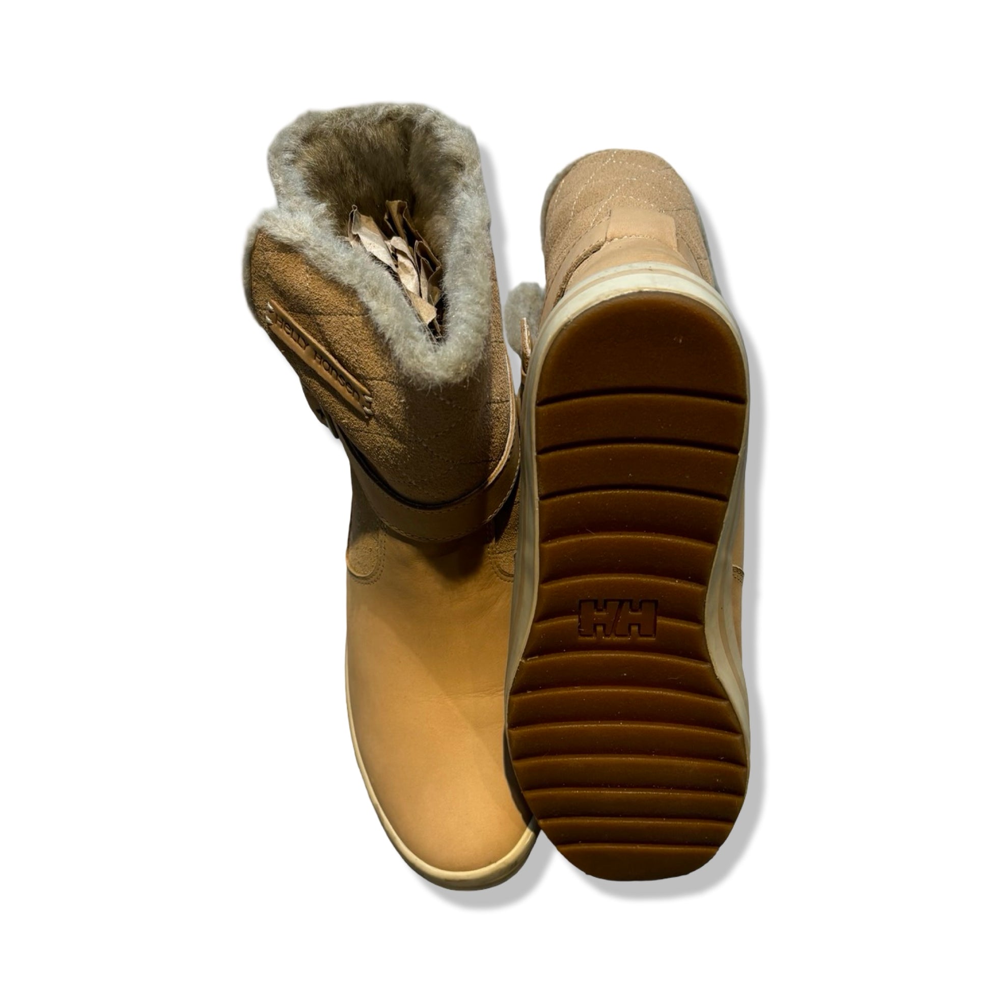 Helly Hansen vinterkängor för dam i beige. Kängorna är fotograferade ovanifrån och visar ena kängans bruna sula och den andras pälsfodrade insida mot en vit bakgrund.