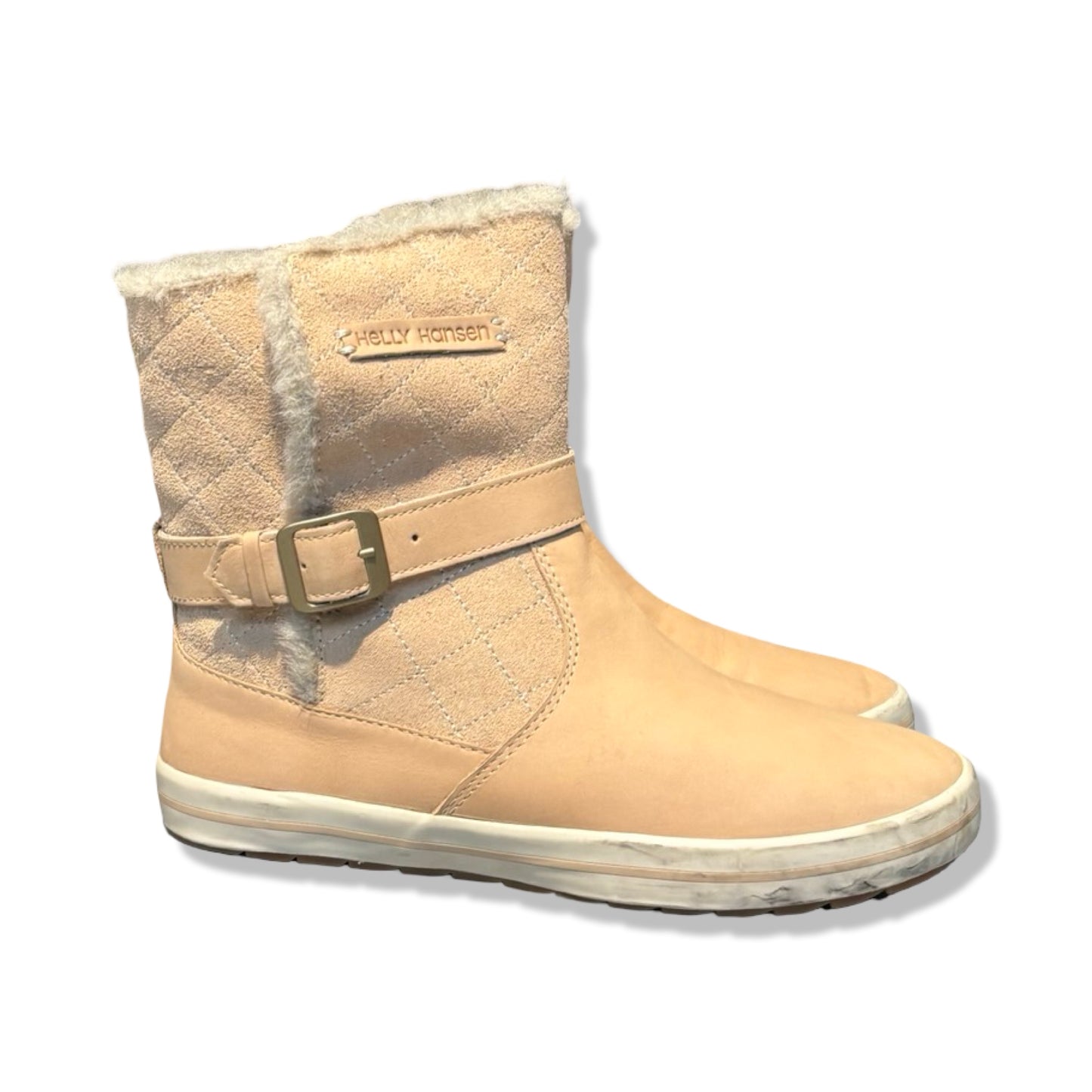 Helly Hansen vinterkängor för dam i beige. Kängorna har kviltat skaft, ljust foder och ett dekorativt spänne och är fotograferade från sidan mot en vit bakgrund.