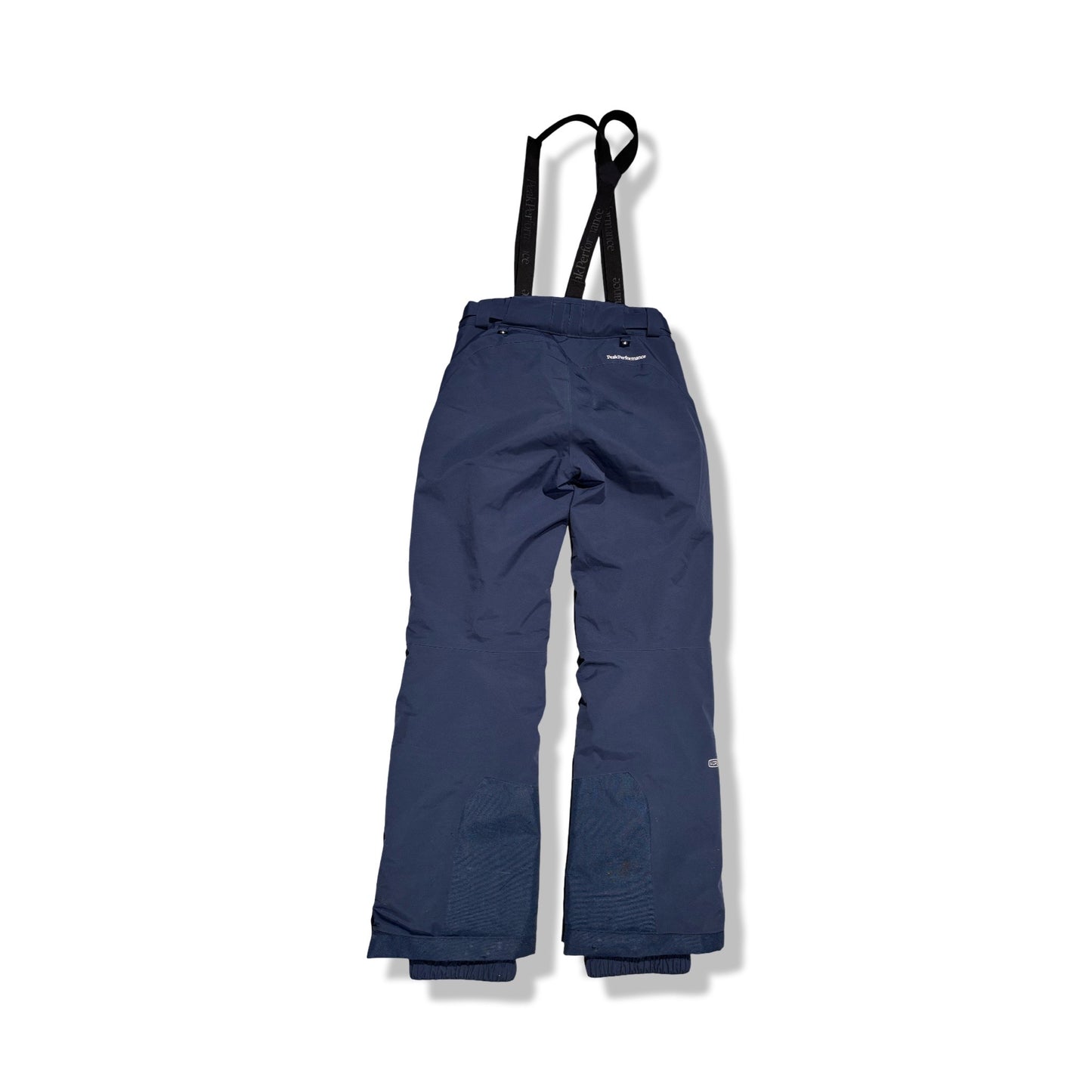 Baksidan av Peak Performance skidbyxa för dam i mörkblått med svarta hängslen, fotograferad platt mot en vit bakgrund.